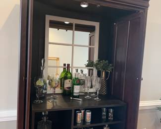 Former entertainment center turned into ‘The Instant Speakeasy’!
Unit is 22”deep, 41”wide, 81”tall. &nbsp;Lighting inside for highlighting items. Dark cherry finish.
21-Piece Home Bar Transformation includes 2 decanters, 7 crystal flutes, 5 hand painted wine glasses, tongs, 2 crystal highball glasses, 1 crystal candy/ nut dish, 2 shot glasses 1 white mirror, 1 faux plant in ceramic vase.&nbsp;
&nbsp;