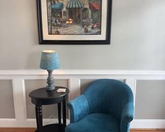 "A curated three-piece interior vignette featuring a plush teal velvet club chair 29w 33d 31h with mahogany look finished legs, paired with a classic black oval pedestal side table 19w 15d 27.5h
Accompanied by a large-scale framed 38x32h
Mediterranean street scene print that harmonizes the cool blues and warm neutrals of the collection. A cozy
ready-made reading&nbsp;
