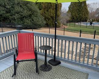 Outdoor rug, red outdoor rocker plus small table and umbrella with stand.
