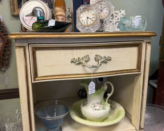 bedside table, clocks, duck cologne bottle, books, framed art