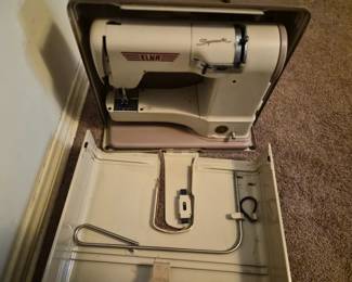 Elna Supermatic sewing machine.
It was manufactured by Tavaro of Switzerland, starting in the early 1950s. 
The machine features durable metal construction and a compact design. 
The carrying case converts into an extra-large quilting platform. 
It uses Elna discs (cams) to provide a variety of decorative stitches. 
These models often include a knee lever for speed control instead of a foot pedal. 
