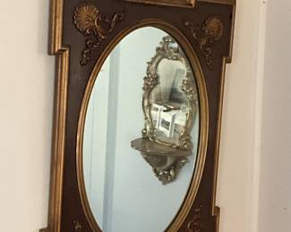 Round mirror inside gold colored frame with motifs in each corner