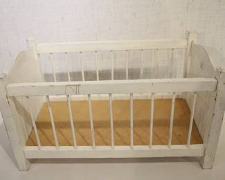 A white, distressed wooden doll crib, 21" x 12" x 14". This item can be shipped.