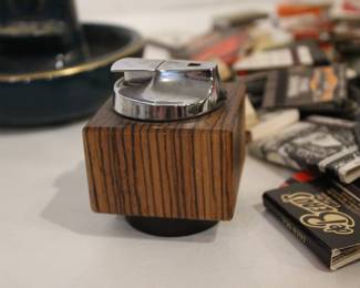 vintage Ronson Varaflame "Ambassador" table lighter with a chromed steel top and a Brazilian rosewood (or similar wood) cube-shaped base 3" x 3" in a lot with a black and gold ceramic ash tray 6" x 4", and a large pile of vintage matches. These items can be shipped.