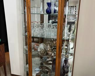 Howard Miller curio cabinet full of crystal, porcelain, glass, and silverplate.