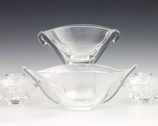 Four pieces of mid 20th century Steuben Crystal tableware.  Includes a shape no. 8068 "boat shaped" bowl, a shape no. 7970 oval bowl, and a pair of shape no. 8081 low candlesticks.  Each with etched "Steuben" signatures at underside.  Minor surface wear, boat shaped bowl with a few tiny flakes, some scratches to undersides.  Up to 11 3/4" long and 4 1/2" high.