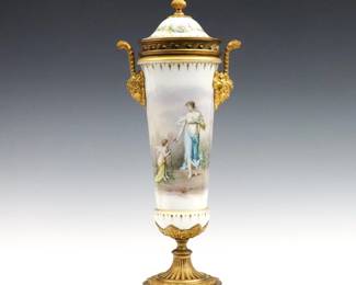 A late 19th century French Sevres style porcelain covered urn.  Tapered form with figural scenic decoration depicting a woman and Cherub on a White ground, with Gilded Bronze mounts and Bacchus mask handles.  Signed by the artist "V. Fecatte".  Some wear to Gilded finish, one handle loose, covered adhered.  17 1/2" high.  NOTE: From the estate of Bill & Barbara Shulhof of Saginaw, Michigan.