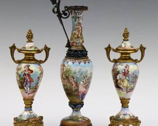 Three turn of the century Viennese miniature enameled vases.  Hand-enameled scenic decoration depicting ladies, gentleman and cherubs, on Gilded metal mounts.  Includes a pair of covered urns and a baluster vase with cast handle.  Some wear to Gilded patina particularly on tall single vase.  Up to 6 1/2" high.   NOTE: From the estate of Bill & Barbara Shulhof of Saginaw, Michigan.