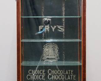 A turn of the century Fry's Chocolates wall hanging store display cabinet.  Walnut construction features an arched crown with porcelain advertising panel reads "Frys's Chocolate" over a single long glass door with reverse painted advertising and four glass interior shelves.  Maker's tag on back "R. Palmer Maker, Bristol".  Original finish with some wear.  21 x 7 x 44 1/2" high overall.  
