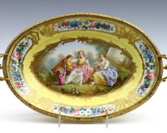 A late 19th century French Sevres style mounted porcelain center bowl.  Oval porcelain dish with Romantic scenic decoration and floral borders on a Yellow ground, mounted on a Gilded Bronze frame with two scrolled handles, floral garland apron and flared feet.  Painted Sevres style Interlacing L's mark with enclosed "A" above "S..".  Minor wear to decoration, some wear to Gilded finish.  15 1/2 x 8 1/2 x 6 1/2" high overall.  NOTE: From the estate of Bill & Barbara Shulhof of Saginaw, Michigan.