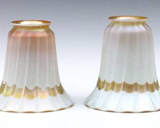 A pair of early 20th century Quezal Art Glass shades.  Flared Iridescent White glass forms with Gold pulled linear decoration.  Signed "Quezal" at fitters.  Minor surface wear.  Each 5" high with 2 1/8" fitters.   NOTE: From the estate of Bill & Barbara Shulhof of Saginaw, Michigan.