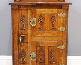 A turn of the century American Icebox.  Oak construction with applied carving features a shaped mirrored backsplash over lift top compartment with partial paper label, above two paneled doors,  Brass hardware and cold water tap.  Refinished with minor wear.  28 x 18 x 48" high. 