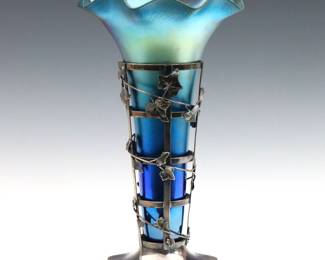 A turn of the century Art Glass vase with Pairpoint Silverplate base.  Features a trumpet form Iridescent Blue glass insert with ruffled rim, on a Silverplate base with pierced lattice design and cast ivy decoration.  Based marked "Pierpoint MFG Co." and "Quadruple Plate / 592".    Minor wear, two Silverplate leaves with damage.  13 1/4" high.   NOTE: From the estate of Bill & Barbara Shulhof of Saginaw, Michigan.