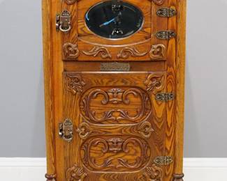 A turn of the century American "Belding's National" Icebox.  Oak construction with extensive applied carving features a paneled lift top above two hinged doors, the upper with an oval beveled mirror flanked by Griffin topped columns with paw feet, Brass hardware and nameplate.  Refinished with minor wear.  28 x 18 x 53 1/2" high.  