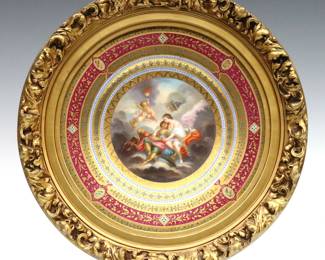 A turn of the century framed Royal Vienna porcelain cabinet plate.  Hand-painted Neoclassical depiction of a couple and Putti lounging among heavenly clouds surrounded by multiple floral borders with Gilded detail.  Blue underglaze Bindenschild or Beehive mark.  Hairline to edge, only visible at back.  Image 9" diameter, in a carved wooden frame re-painted gold with minor shrinkage, 12 1/2" diameter.  NOTE: From the estate of Bill & Barbara Shulhof of Saginaw, Michigan.