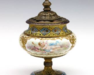A turn of the century French Sevres style covered urn.  Porcelain body with bulbous form and hand-enameled Cupid decoration on Champleve Bronze mounts with cast Bronze cover.  Minor wear to decoration, wear to Gilded patina, cover may be a replacement.  6 1/2" high.   NOTE: From the estate of Bill & Barbara Shulhof of Saginaw, Michigan..