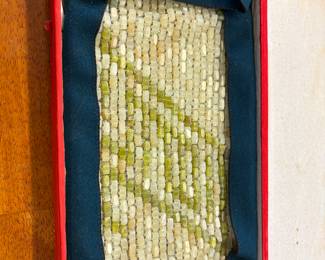 Numerous small, polished Xiuyan jade beads (or similar stone) woven together.  The beads display a range of light green and yelowish-white colors,