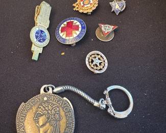 collection of vintage pins, badges, and a medallion keychain