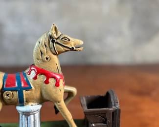 This lot features a reproduction cast iron mechanical bank known as the "Trick Pony". This bank measures, 7” H x 7” W x 2.5” D. The bank was originally patented in 1885 by Juleus Mueller, with manufacturing rights assigned to Charles and Walter Shepard. To operate the bank, a coin is placed in a small trough on the left, and a lever is pulled. 

