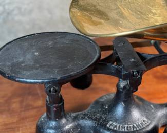 This lot features an antique Fairbanks cast iron balance scale with a brass scoop pan/hopper and a separate platform for weights (included). This scale (without hopper) measures, 9” H x 16” W x 5” D.

