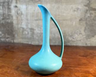 This lot features a stunning Van Briggle art pottery ewer (pitcher) in a matte turquoise glaze. The ewer has a distinct tear-drop or bulbous body shape with an integrated, flowing handle. Van Briggle pottery is a renowned name in American art pottery, known for its Art Nouveau designs and unique glazes. This pitcher measures, 11.5” H x 7” W x 6” D.

