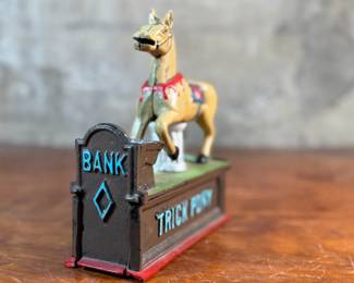 This lot features a reproduction cast iron mechanical bank known as the "Trick Pony". This bank measures, 7” H x 7” W x 2.5” D. The bank was originally patented in 1885 by Juleus Mueller, with manufacturing rights assigned to Charles and Walter Shepard. To operate the bank, a coin is placed in a small trough on the left, and a lever is pulled. 

