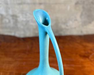 This lot features a stunning Van Briggle art pottery ewer (pitcher) in a matte turquoise glaze. The ewer has a distinct tear-drop or bulbous body shape with an integrated, flowing handle. Van Briggle pottery is a renowned name in American art pottery, known for its Art Nouveau designs and unique glazes. This pitcher measures, 11.5” H x 7” W x 6” D.

