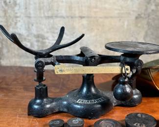 This lot features an antique Fairbanks cast iron balance scale with a brass scoop pan/hopper and a separate platform for weights (included). This scale (without hopper) measures, 9” H x 16” W x 5” D.

