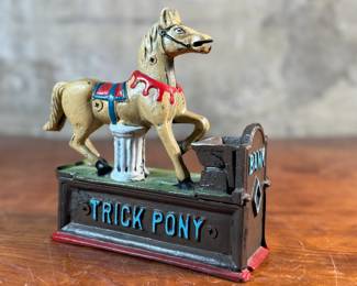 This lot features a reproduction cast iron mechanical bank known as the "Trick Pony". This bank measures, 7” H x 7” W x 2.5” D. The bank was originally patented in 1885 by Juleus Mueller, with manufacturing rights assigned to Charles and Walter Shepard. To operate the bank, a coin is placed in a small trough on the left, and a lever is pulled. 

