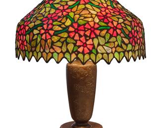 1262
A Handel leaded glass table lamp
Early 20th century
Shade aperture ring marked: Handel pat. no. 924457; base marked: HANDEL
The patinated metal base in the style of a Japanese vase, with floral motifs in relief, issuing three lights and surmounted by a leaded glass shade depicting violets
Shade: 9.625" H x 17" Dia.; Base: 23.375" H x 6.875" Dia.
Estimate: $3,000 - $5,000