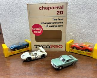Two - Aurora model motoring HO scale slot cars (in their original yellow ‘garage’), white Tycopro HO scale #66 slot car, light green Ford Mustang Fastback HO slot car (missing one tire).