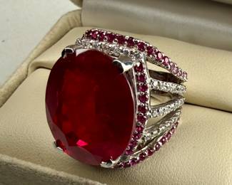 This lot features a statement piece! A large 30+ carat oval ruby cocktail ring set in sterling silver with diamonds and sapphires. This ring comes in a size 5.5 with a total approx. weight of 14.64 grams.

