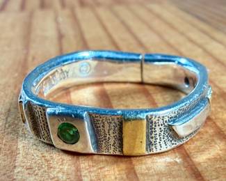 This lot features a hand made ring by maker, Armstrong. The ring is crafted from sterling silver and 22k gold. This ring comes in a size 10, a broken band as shown in photos, and a total approx. weight of 5.66 grams.

