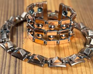 This lot features a necklace and bracelet by Renoir Copper. The necklace measures, 15” and the bracelet, 6.5”. Renoir copper jewelry is a highly collectible mid-century costume line produced by Jerry Fels in California from 1946 to 1964. Renowned for its abstract, modernist, and Arts & Crafts-inspired designs, the company specialized in solid, hand-hammered copper, frequently featuring bold, minimalist forms. 

