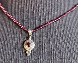 This lot features a vintage garnet beaded necklace with a sterling silver pendant containing a single garnet stone. This necklace measures, 17”.

