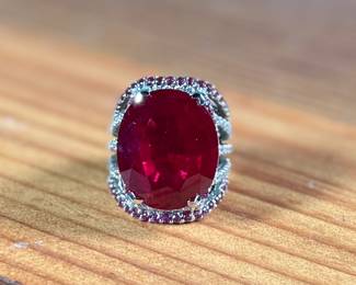 This lot features a statement piece! A large 30+ carat oval ruby cocktail ring set in sterling silver with diamonds and sapphires. This ring comes in a size 5.5 with a total approx. weight of 14.64 grams.

