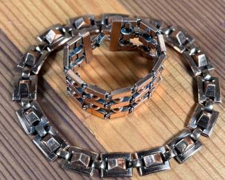 This lot features a necklace and bracelet by Renoir Copper. The necklace measures, 15” and the bracelet, 6.5”. Renoir copper jewelry is a highly collectible mid-century costume line produced by Jerry Fels in California from 1946 to 1964. Renowned for its abstract, modernist, and Arts & Crafts-inspired designs, the company specialized in solid, hand-hammered copper, frequently featuring bold, minimalist forms. 

