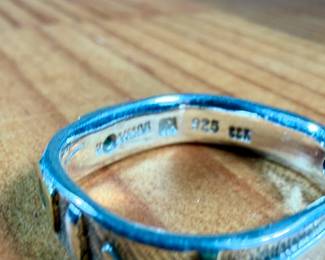 This lot features a hand made ring by maker, Armstrong. The ring is crafted from sterling silver and 22k gold. This ring comes in a size 10, a broken band as shown in photos, and a total approx. weight of 5.66 grams.

