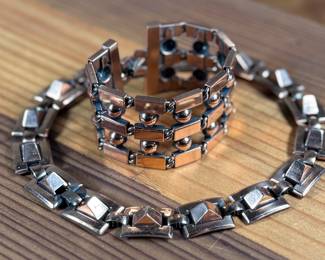 This lot features a necklace and bracelet by Renoir Copper. The necklace measures, 15” and the bracelet, 6.5”. Renoir copper jewelry is a highly collectible mid-century costume line produced by Jerry Fels in California from 1946 to 1964. Renowned for its abstract, modernist, and Arts & Crafts-inspired designs, the company specialized in solid, hand-hammered copper, frequently featuring bold, minimalist forms. 

