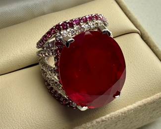This lot features a statement piece! A large 30+ carat oval ruby cocktail ring set in sterling silver with diamonds and sapphires. This ring comes in a size 5.5 with a total approx. weight of 14.64 grams.

