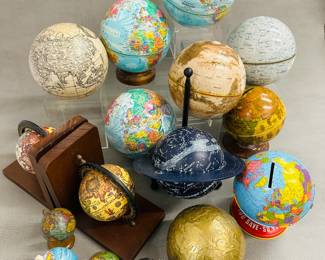A collection of vintage globes, some of which are tin globe banks from companies like Ohio Art and J. Chein; one pair of globe bookends, and a dark blue universal celestial star globe designed to help identify constellations. 
