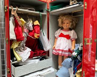 A vintage Shirley Temple Dress Up Doll in a red trunk containing multiple outfits. 
