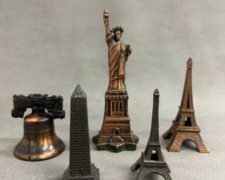 Vintage cast metal souvenir figurines of famous landmarks including miniatures of the Statue of Liberty, the Washington Monument, the Liberty Bell, and two models of the Eiffel Tower. 
