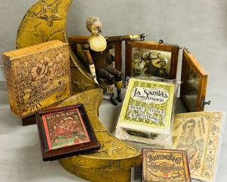 Antique and vintage display and advertising items including a small, jointed wooden doll; an antique Hastings & Co. Gold Leaf box that contains real gold leaf sheets, a hand-made lidded wooden handkerchief box with burned surface design of poppies against a checkered background, a set of gold-toned half moon-shaped nesting boxes, a vintage box of "La Sanilas" brand pure tissue paper