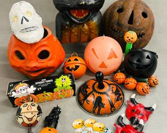 Vintage Halloween decorations and toys including an Avon Spooky Tunes Light-up Musical Bracelet, a vintage 1940s/1950s paper mâché black cat Halloween decoration, a vintage tin litho Halloween noisemaker or clanger decorated with black cat, owl, and flying witch; a set of small Jack-o-lantern metal bells, vintage hand-painted Mexican folk art devil masks, a Jack-O-Lantern PEZ dispenser and a candle