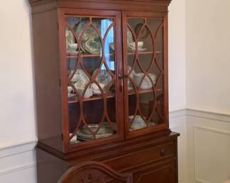Full picture of the China cabinet with beautiful try and flower arrangement on top.