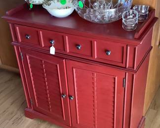 Cute red cabinet with shutter like doors with drawers and shelf.