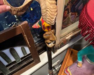 decorative walking cane featuring a hand-carved face with a large horn and colorful fabric accents