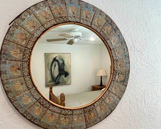 This round wall mirror features a distinctive, wide frame adorned with a repeating embossed pattern
