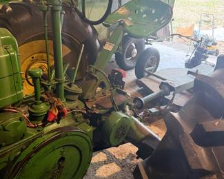 Vintage John Deere Model B tractor  A classic piece of agricultural machinery manufactured between 1935 and 1952.   John Deere B with a large exposed flywheel on the side. Equipped with a manual transmission and a power take-off (PTO) shaft for running implements. Gated gear shifter, heavy-duty metal pedals, and traditional mechanical controls with a distinctive two-cylinder design.